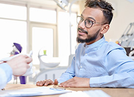 man with glasses talking to dentist