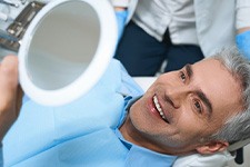 a patient smiling and checking his teeth with a mirror