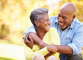 Man in blue shirt hugging woman in yellow sweater outside smiling